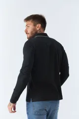 Polo de manga larga negra con cuello clásico, tapeta de dos botones y bolsillo de parche en el pecho con ribete blanco. Logo de la marca bordado en blanco sobre el bolsillo.