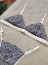 Conjunto de lencería compuesto por un corpiño triangular y una bombacha tipo tanga, confeccionados en encaje gris con detalles de terminaciones en color champagne.