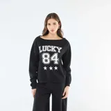 Buzo de felpa color negro con cuello redondo amplio y mangas largas. Presenta un estampado frontal en color blanco con la palabra 'LUCKY', el número '84' y tres estrellas.