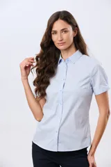 Camisa celeste rayada de manga corta, con cuello camisero y cierre frontal con botones. Presenta un corte entallado y un pequeño detalle de placa metálica en el borde inferior.
