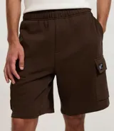 Bermuda masculina color marrón oscuro, confeccionada en tela French Terry, con cintura elástica y cordón de ajuste. Presenta bolsillos cargo funcionales a los lados.