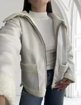 Campera corta color crudo de ecocuero con interior de corderito, cierre frontal con cremallera y bolsillos laterales.