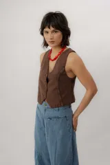 Chaleco de denim azul con cuello en V, cierre frontal con botones metálicos y pespuntes en contraste.