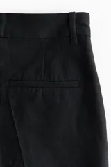 Short negro de tiro alto en mezcla de lino, algodón y viscosa, con pliegues frontales y posteriores, bolsillos al bies y bajos con vuelta cosida.