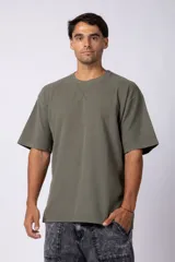 Remera de corte oversized en color marrón, confeccionada en tejido de algodón con textura de micropanal. Presenta cuello redondo con detalle de costura en forma de X y mangas cortas de estilo caído.
