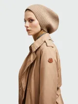 Gabardina de plumas color beige, con capucha, cierre frontal con botones y cinturón ajustable.