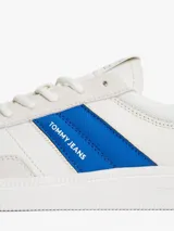 Zapatillas deportivas de estilo vintage Tommy Jeans modelo The Greenwich, confeccionadas en ante color blanco con paneles laterales en azul vibrante y detalles en gamuza gris claro. Presentan cierre con cordones, suela cupsole de goma y logo de la marca en el lateral.