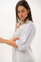 Vestido corto off-white con escote en V, de corte recto y holgado. Cuenta con mangas abullonadas tres cuartos confeccionadas en tejido broderie.
