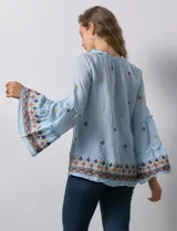 Blusa celeste de gasa bordada, con escote en V y lazo de ajuste. Mangas largas con terminación amplia.