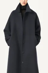 Tapado largo de corte amplio en color azul marino, confeccionado en una mezcla de poliéster y lana. Presenta un diseño con cuello camisero, cierre frontal mediante botones y puños con cintos regulables para un ajuste personalizado.