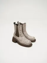 Bota tipo chelsea de cuero vacuno en color rojo con estampado floral grabado en negro. Presenta paneles laterales elásticos, suela de plataforma y taco cuadrado en color negro.