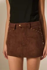 Minifalda marrón de gamuza sintética con tiro alto y detalles de tachas doradas a lo largo de los costados y bolsillos delanteros.