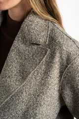 Tapado largo de corte oversize en color beige, con solapas clásicas y cierre frontal con botones. Presenta un diseño minimalista y elegante, ideal para un look sofisticado.