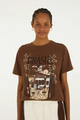 Remera marrón de manga corta y cuello redondo, con estampa frontal temática de Brasil que incluye palmeras, arquitectura colonial y aves.