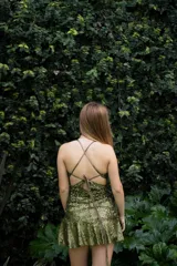 Vestido corto negro con estampado de plumas doradas, escote en V, breteles finos cruzados en la espalda, cut-outs laterales y volado en el ruedo.