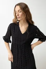 Vestido largo negro con tejido calado tipo broderie inglés, escote en V, mangas cortas con volado y diseño de capas con volados en el ruedo.