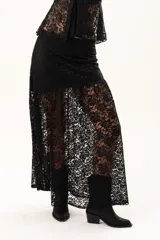 Pollera larga de encaje negro con diseño asimétrico. Presenta un forro interno hasta la altura del muslo y una sección inferior con transparencias que aporta movimiento y fluidez.