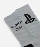Medias de caña alta color gris con detalles en negro en la puntera, talón y planta del pie. Presentan el logo de Playstation y el texto 'player one' estampado en el lateral.