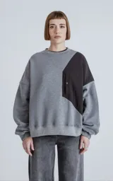 Buzo de cuello redondo con diseño oversize y corte crop. Presenta una combinación de colores gris melange y negro, con un bolsillo frontal técnico de microfibra con cierre a presión.