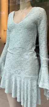 Vestido corto negro de encaje con escote en V, mangas largas acampanadas y falda con volado en el ruedo.