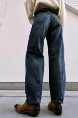 Jeans de tiro medio, color azul oscuro lavado, con corte balloon fit (holgado en muslos y estrechado en el tobillo). Presenta cinco bolsillos, cierre frontal con botones y detalle de trabilla con hebilla en la parte trasera de la cintura.