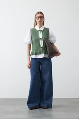 Chaleco tejido color verde musgo, con trama texturada, cuello a la base y cierre frontal con lazos. Presenta un ruedo con volado.