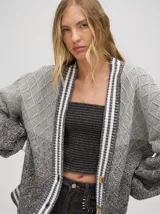 Cardigan oversize de algodón con diseño tejido a rombos en tonos degradados de marrón y blanco. Presenta cuello en V, cierre frontal con botones de madera y puños y dobladillo con rayas blancas.