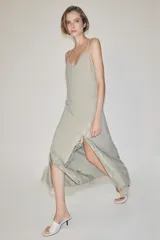 Vestido largo lencero de tejido fluido en color gris verdoso, con escote en V, tirantes finos y detalles de encaje a tono en el bajo y los laterales, además de una abertura frontal.
