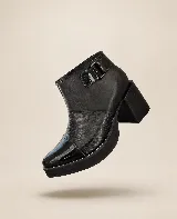 Botin negro con plataforma y taco ancho, confeccionado con una combinación de texturas que incluye puntera de charol, panel texturizado tipo reptil en el empeine y cuero liso en la caña. Cuenta con detalle de tira con hebilla lateral.