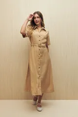 Vestido camisero largo color beige, con cuello clásico, mangas cortas, cierre frontal con botones y cinturón con hebilla veteada.