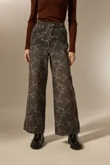 Pantalon de jean estilo baggy con estampado floral en tonos gris oscuro y blanco. Presenta un corte de pierna ancha, tiro medio y cierre frontal con botón y cremallera.