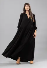 Vestido largo negro con escote en V y detalle de frunces en los hombros. Tiene mangas largas con elástico en los puños y volados en el ruedo.