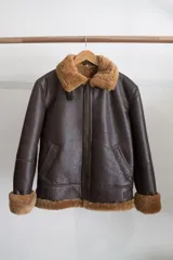Campera tipo bomber de cuero genuino color negro, con interior y cuello de piel sintética negra. Presenta cierre frontal metálico, bolsillos laterales y puños con terminación en tejido acanalado.