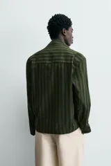 Sobrecamisa de hombre con cuello solapa, manga larga y cierre frontal de botonadura. Presenta un estampado de rayas verticales en tonos de verde oliva y verde oscuro. Incluye bolsillos plastrón en la cadera.