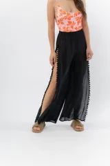 Pantalón ancho de gasa liviana color blanco, con cintura elástica y aberturas laterales decoradas con pompones.