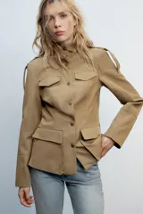 Cazadora de estilo militar en color tostado, con cuello subido, cierre frontal con botones y múltiples bolsillos con solapa en el pecho y la cintura. Cuenta con mangas largas con trabillas en los hombros.