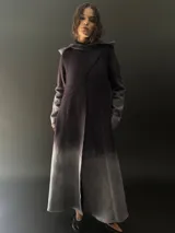 Tapado largo de lana merino color gris oscuro con teñido degradado en gris claro en ruedo, mangas y capucha. Tiene corte recto, bolsillos laterales y cierre cruzado con broches a presión ocultos en los hombros.
