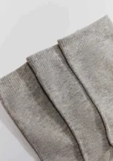 Kit de tres pares de medias unisex de caño medio, confeccionadas en tejido suave y elástico de color blanco, con el logo de la marca estampado en la planta del pie.