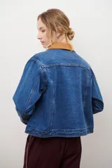 Chaqueta de jean azul con cuello de gamuza color camel, bolsillos delanteros y cierre de botones.