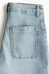 Jean de denim de algodón con tiro alto y pierna amplia de estilo wide leg. Presenta bolsillos tipo parche en la parte delantera y un lavado claro con efecto desgastado.
