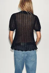 Polo negro de punto calado con cuello clásico, manga corta abullonada y terminación ondulada en el ruedo.