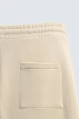 Bermuda de algodón color beige, estilo jogger, con corte relajado, cintura elástica ajustable con cordón y bolsillos laterales y trasero.