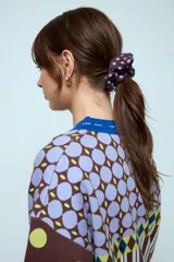 Gomita de pelo tipo scrunchie de tela, con diseño de lunares en tonos marrón y lila.