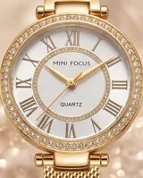 Reloj de pulsera analógico con caja redonda de metal dorado y bisel con incrustaciones de cristales. Esfera blanca con números romanos y malla de acero tipo milanesa en tono dorado.