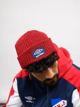 Gorro tipo beanie de punto acanalado en color azul, con parche frontal bordado que incluye el logo de Umbro y la palabra Nacional.