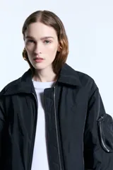 Campera tipo bomber de nylon con ligero relleno, corte cropped y ajuste recto. Presenta cuello camisero, cierre frontal metálico, puños de ribb y bolsillos frontales con tapa. Incluye un bolsillo decorativo con cierre en la manga y bordado a tono en el frente.