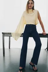 Jeans de tiro alto con corte flare y ajuste slim. Presenta trabillas en la cintura, bolsillos delanteros con detalle de botones metálicos y raya planchada a lo largo de las piernas. Cierre frontal con cremallera y botón.