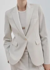 Blazer sastre entallado color beige, con cuello en pico, solapas de muesca, manga larga y bolsillos con solapa en la parte delantera.