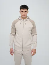 Campera con capucha Umbro modelo Terrace, color beige con bloques en tono tostado en las mangas, cierre frontal completo y bolsillos tipo canguro.