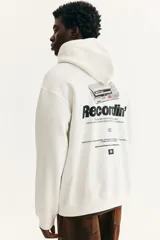 Canguro blanco de mezcla de algodón con interior cepillado suave y estampado frontal negro con la palabra "Recordin'". Tiene capucha de doble capa con cordón ajustable, hombros caídos, bolsillo canguro y puños y bajo acanalados. Corte holgado.